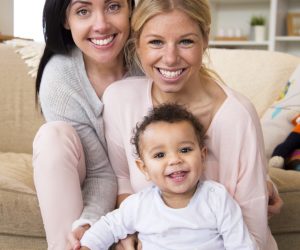 Female couple sit together with their son in their home and all smile for the camera