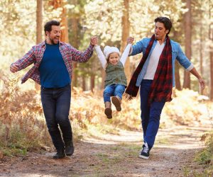 Gay Male Couple With Daughter Walking Through Fall Woodland